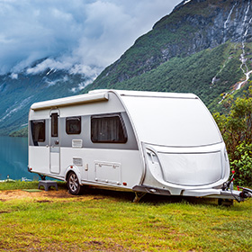 a white caravan parked by a serene lake surrounded by green mountains ideal for 6 campers enjoying nature