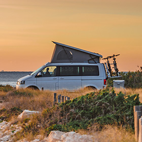 a camper van parked near the coastline at sunset with a bike rack and a beautiful natural background perfect for outdoor adventure