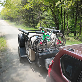 bike racks for five bikes on trailer driving on dirt road through green trees