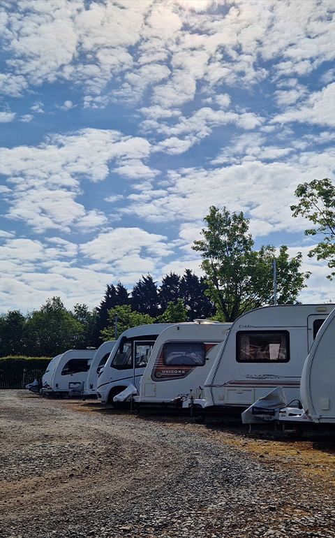 caravans lined up in a campsite under a blue sky with clouds showcasing a perfect spot for eight travelers enjoying outdoor adventures