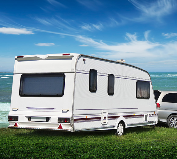 white caravan parked by the ocean under a blue sky with clouds perfect for 2 travelers enjoying outdoor adventure