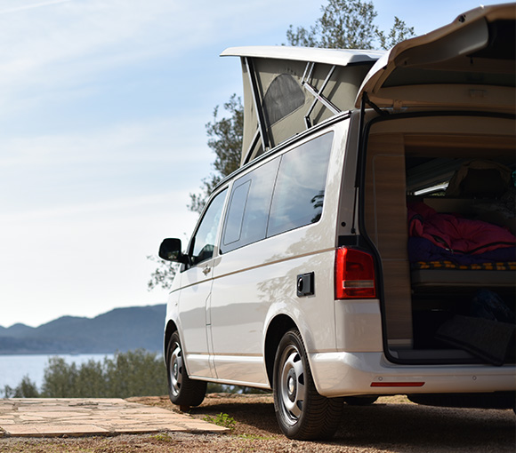 a white camper van parked near a scenic view with a pop-up roof opened showcasing camping gear and a relaxing outdoor atmosphere perfect for three adventurous travelers