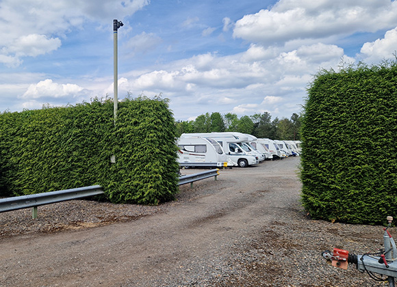 row of parked caravans surrounded by tall green hedges under a cloudy sky ideal for camping and adventures